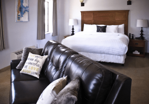 Cozy hotel room featuring a king bed, leather sofa, decorative pillows, and soft lighting.